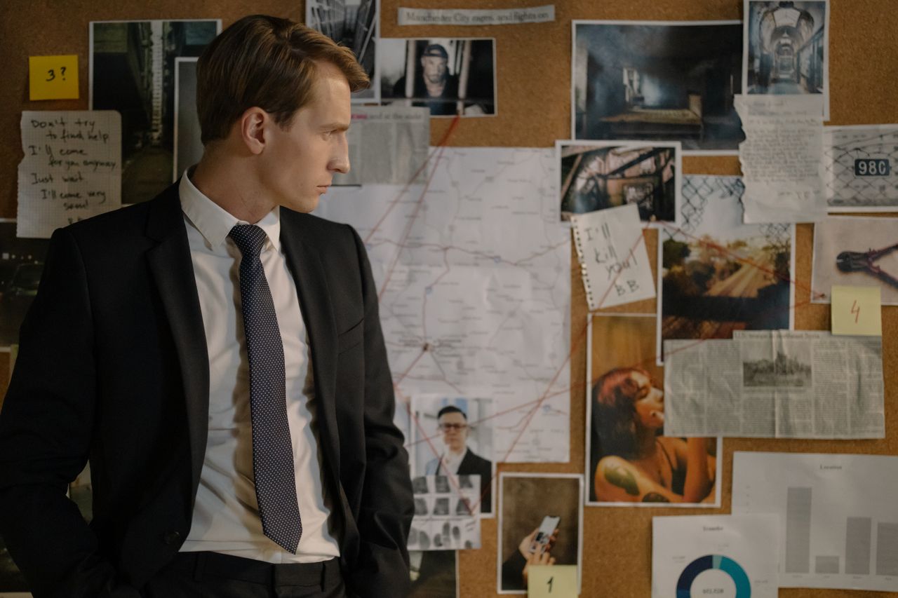 Detective in suit examining evidence on cork board during investigation process.